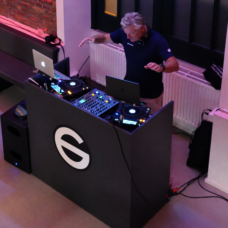 Carsten Esser von Cassollage mit erhobenen Händen hinter seinem DJ-Pult im Glasvoll.